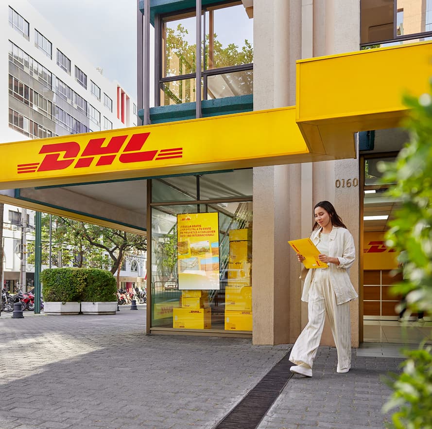 Mujer caminando frente a una tienda de DHL, con un ambiente urbano de fondo.